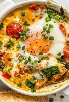 Baked feta eggs with tomatoes and spinach served in a ceramic dish