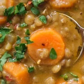 Bowl of vibrant Carrot and Lentil Soup topped with fresh herbs