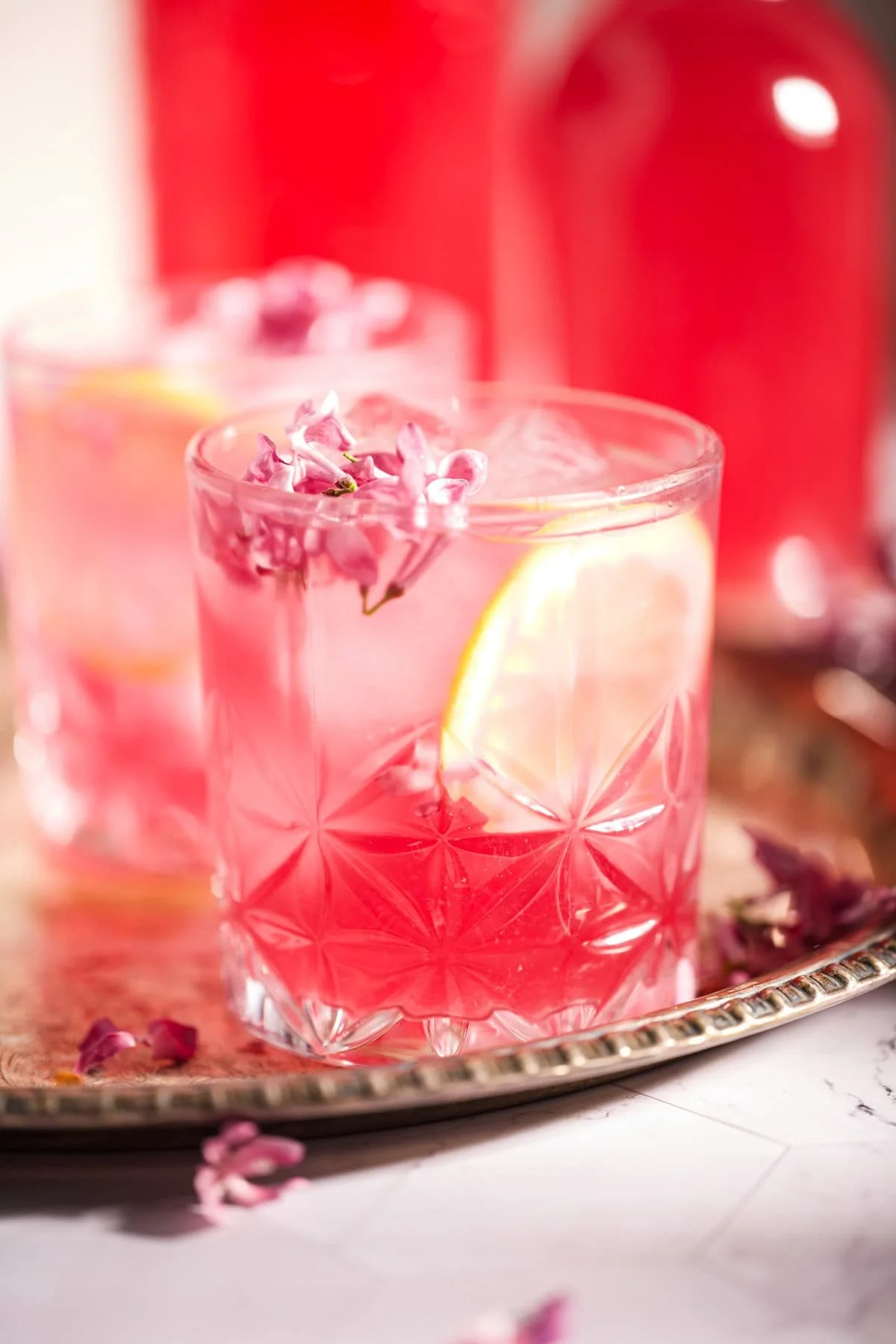 Glass of homemade fermented lilac soda with vibrant lilac flowers.