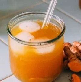 A glass of fermented turmeric soda with vibrant yellow color and frothy texture.