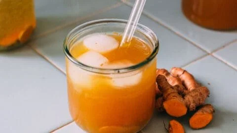 A glass of fermented turmeric soda with vibrant yellow color and frothy texture.