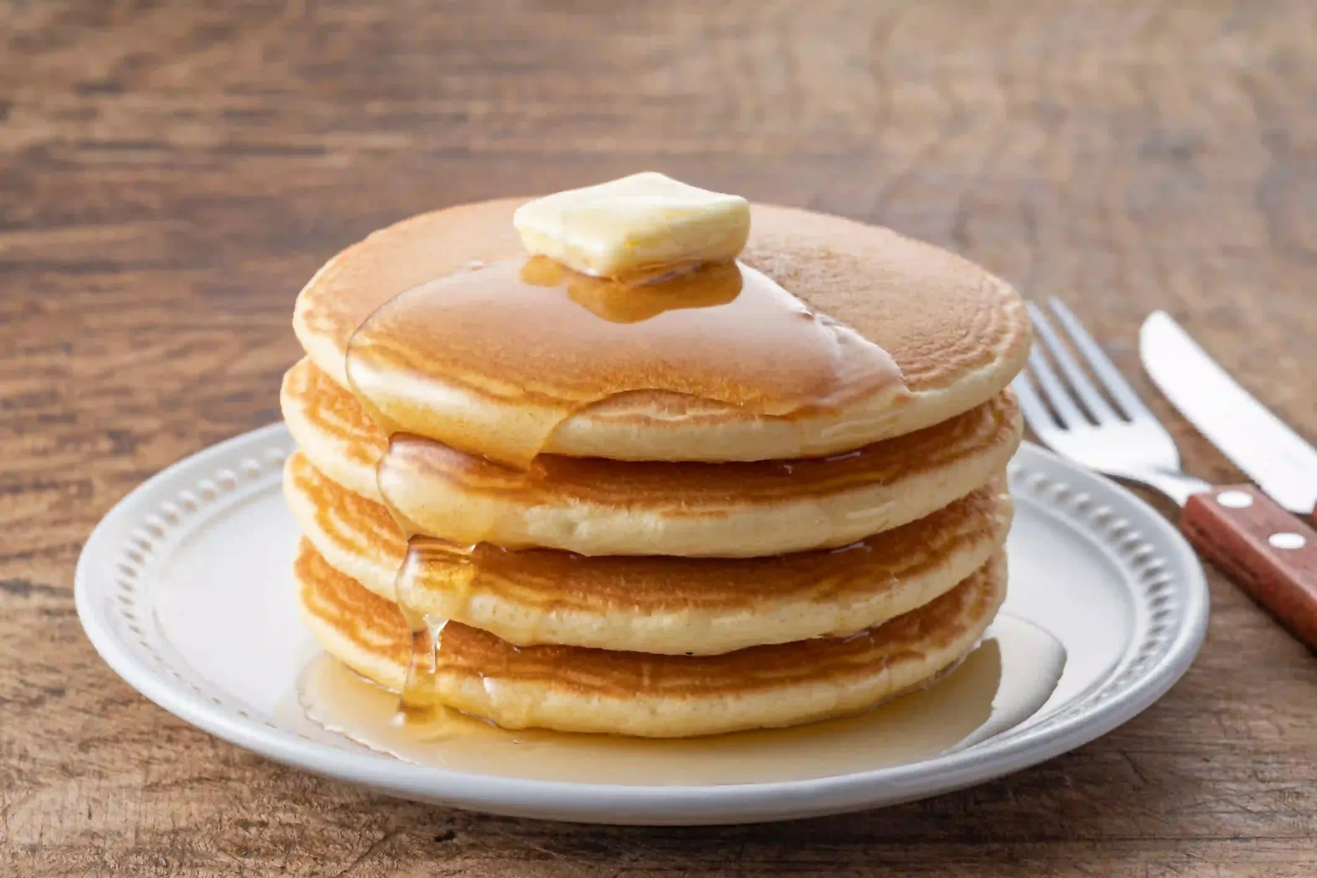 Fluffy buttermilk pancakes stacked on a plate with syrup and berries