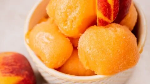 Delicious homemade Peach Sorbet served in a bowl with fresh peaches