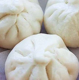Fluffy steamed chicken buns served on a plate, garnished with herbs.