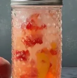 Refreshing homemade strawberry peach soda in a glass with ice and fresh fruit garnish