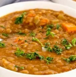 A warm bowl of the best lentil soup topped with fresh herbs and spices.