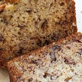 Freshly baked banana bread with bananas on a wooden cutting board