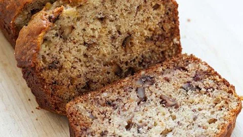 Freshly baked banana bread with bananas on a wooden cutting board