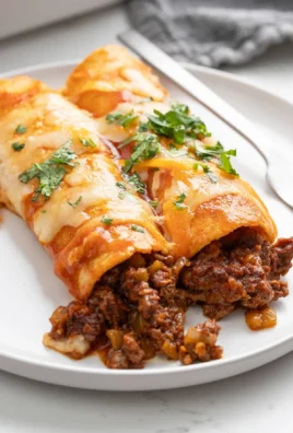 Plate of tasty beef enchiladas topped with cheese and sauce