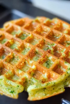 Golden broccoli cheese waffles stacked with melted cheese and fresh broccoli pieces.