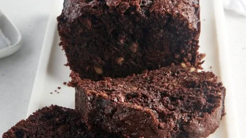 Loaf of chocolate zucchini bread with a slice cut out, showcasing its moist texture.