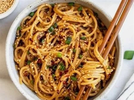 Delicious bowl of Garlic Sesame Noodles topped with sesame seeds and green onions.