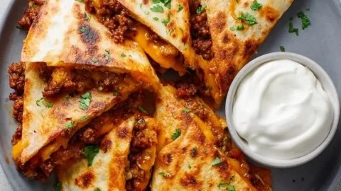 Golden-brown ground beef quesadillas served on a plate with sliced avocado.