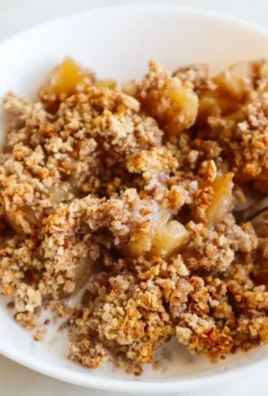Healthy breakfast apple crumble served in a bowl with fresh apples and oats.
