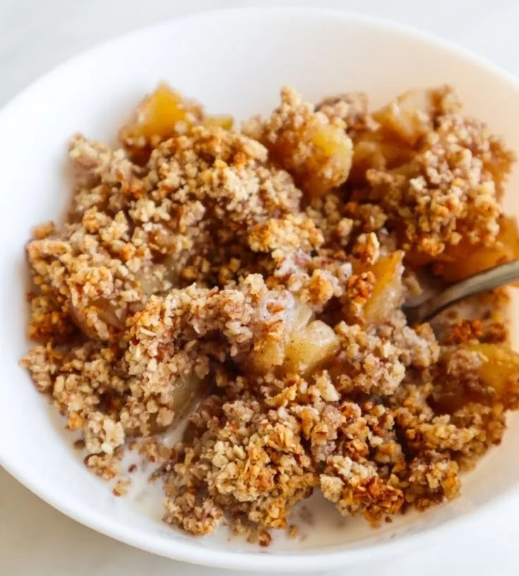 Healthy breakfast apple crumble served in a bowl with fresh apples and oats.