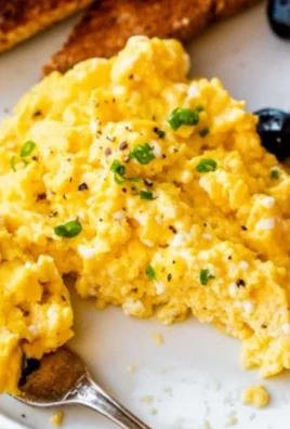 Plate of scrambled eggs with cottage cheese garnished with herbs.