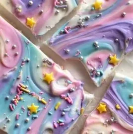 Colorful Unicorn Yogurt Bark topped with sprinkles and fruit on a white plate.