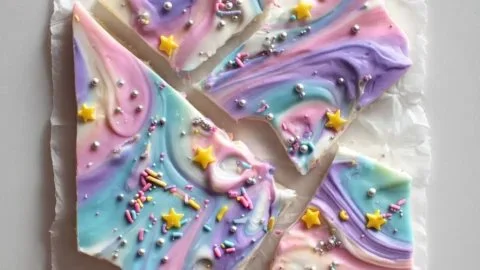 Colorful Unicorn Yogurt Bark topped with sprinkles and fruit on a white plate.